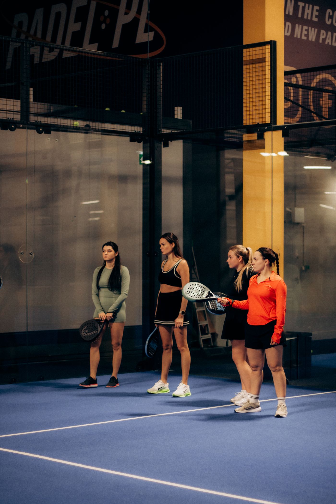 Group playing doubles padel on an indoor glass-walled court