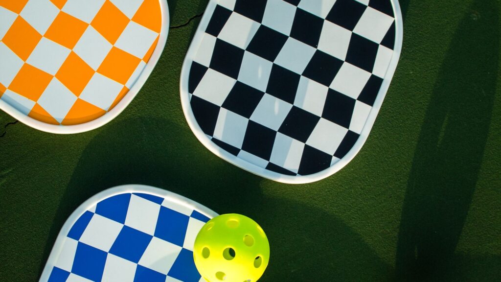 Several pickleball paddles and perforated balls laid flat on a court surface
