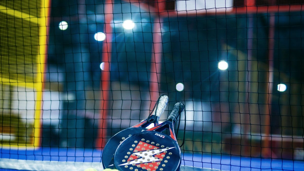 Blue padel court with a racket and yellow balls on the surface