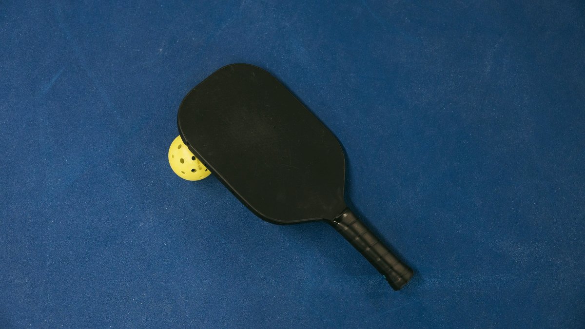 Pickleball paddle and ball resting on a textured blue court surface
