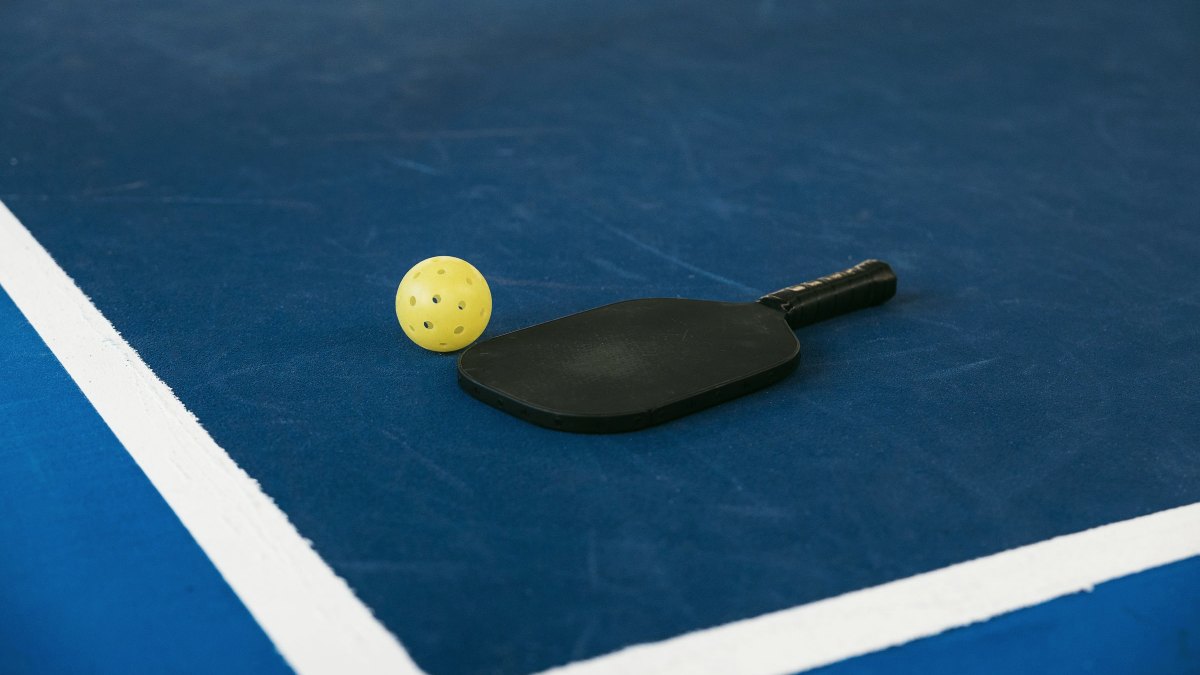 Pickleball paddle and yellow ball on the corner of a blue court