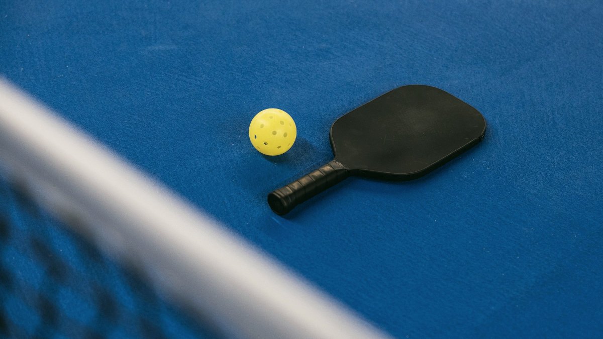 Pickleball paddle and ball resting on a blue court surface