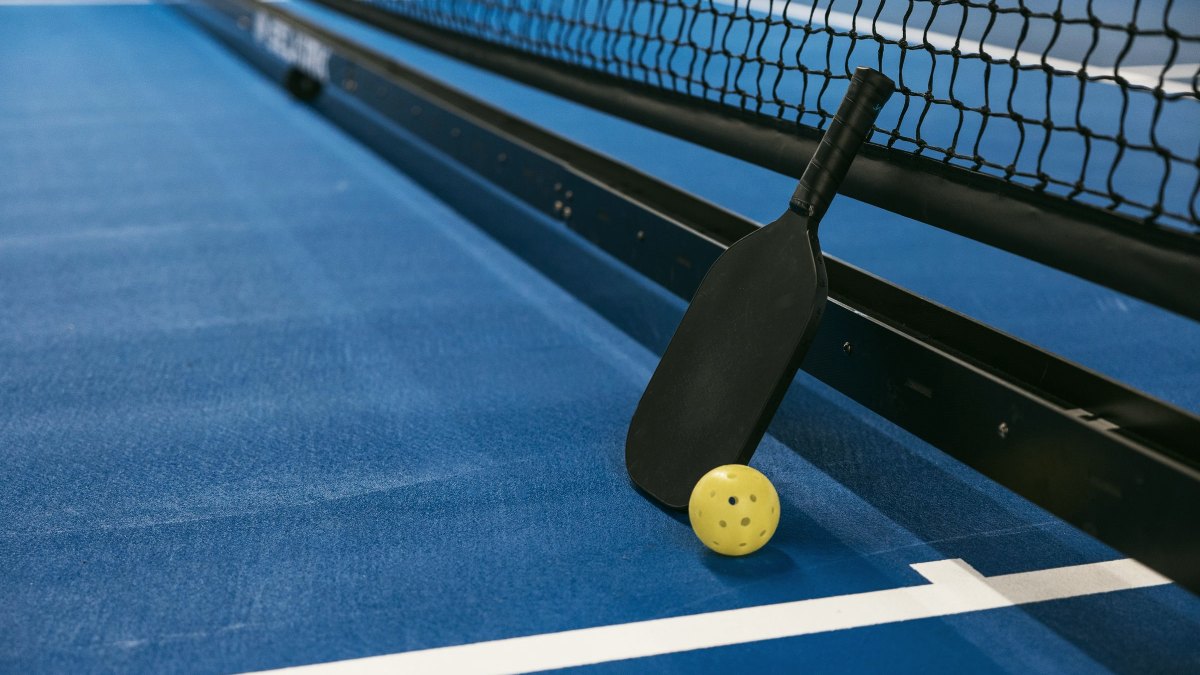 Pickleball paddle and ball resting against the net on a blue outdoor court