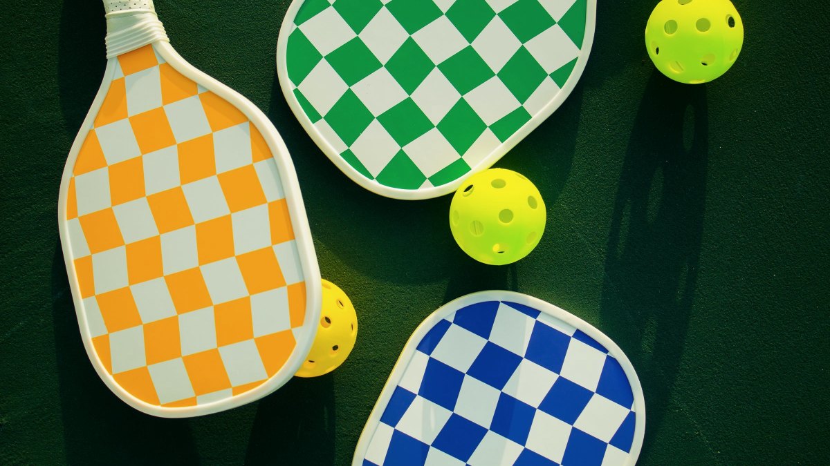 Pickleball paddles and balls arranged on a sunlit outdoor sports court